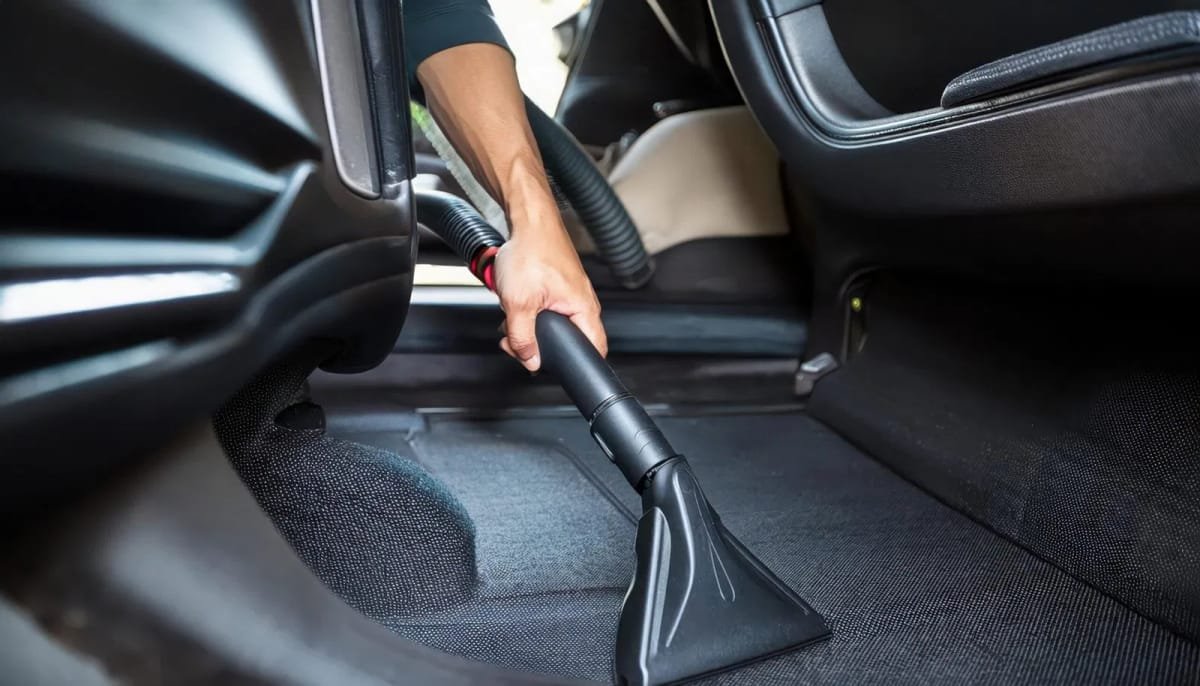 Technician using a commercial-grade vacuum to remove deep-seated debris from vehicle floor mats.