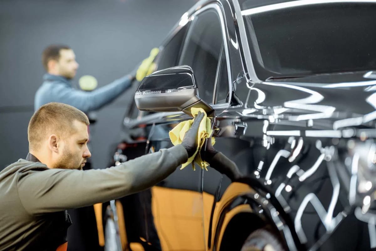 Two technicians meticulously detailing a vehicle's exterior to achieve a high-gloss, showroom finish.